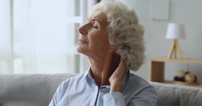 Unhappy tired senior woman rubbing neck feeling pain at home