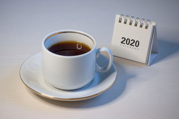 Desk calendar for 2020 on a white table and a cup of coffee.