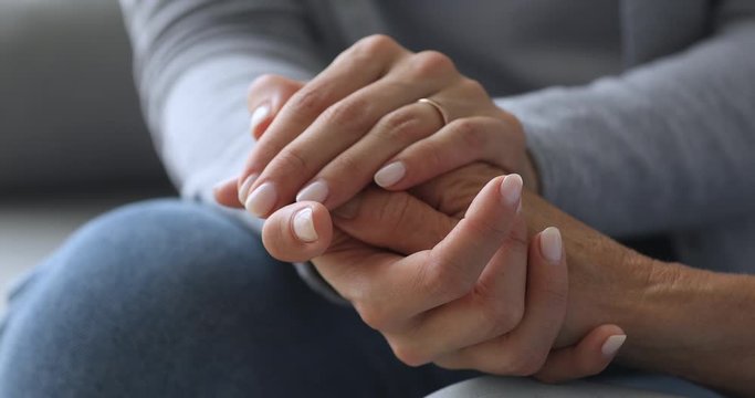 Young woman holding old female hands giving support, close up