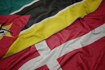 waving colorful flag of denmark and national flag of mozambique.