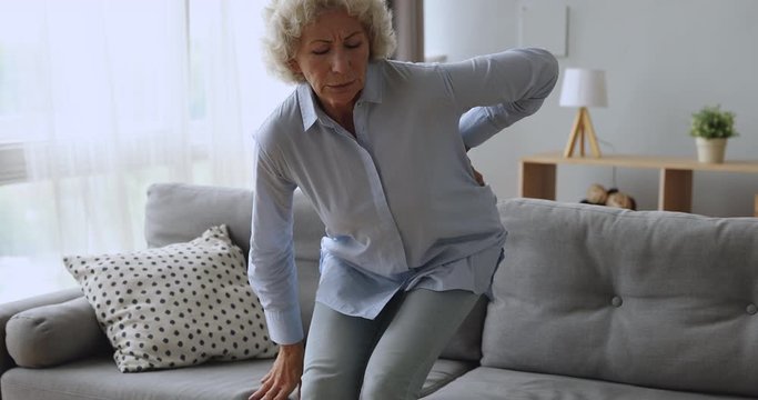 Upset senior woman feel back ache getting up from sofa
