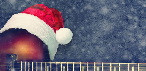 Santa Claus hat on an electric guitar on a blue background. New Year's card for the musician.