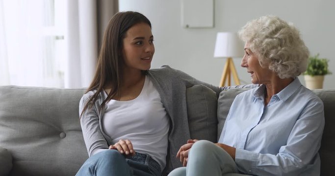 Senior mother and young adult daughter talking sit on sofa