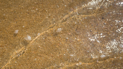 Out of focus photo. Blurred beach sand texture. Golden yellow color background. Sand surface of a beach covered with clear sea water. Waves. 