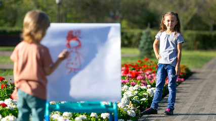Little boy draws his sister as a model. A girl poses as a model to her friend he paints her portrait