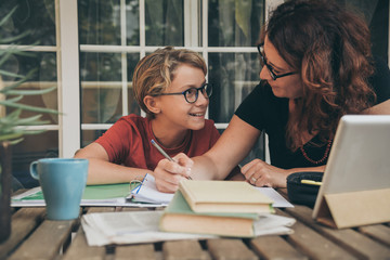 Young student doing homework at home with school books, newspaper and digital pad helped by his...
