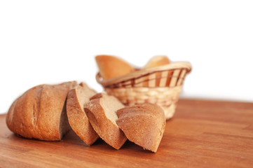 Sliced rye bread and two pies in a wicker basket on a wooden table on a white background
