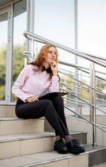 outdoor portrait of a business woman sitting on the stairs looking at the documents