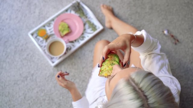 Woman sitting at home in morning light, by the window having an avocado healthy toast. White tray with healthy breakfast background with copy space. Start the day with nutritive food.
