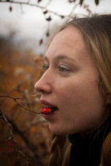autumn portrait of pensive young woman behind the branches of a rosehip bush