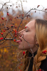autumn portrait of pensive young woman behind the branches of a rosehip bush