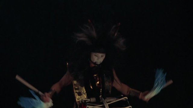 Artist drummer Taiko in a wig with horns and make-up drum on stage against a dark background. Demon from Japanese mythology. 