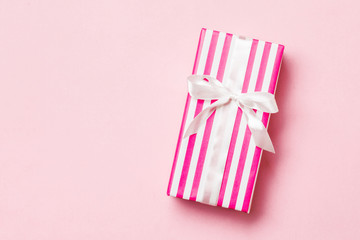 wrapped Christmas or other holiday handmade present in paper with white ribbon on pink background....