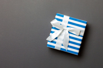 wrapped Christmas or other holiday handmade present in paper with white ribbon on black background. Present box, decoration of gift on colored table, top view with copy space