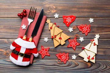 Fototapeta premium Top view of fork and knife tied up with ribbon on napkin on wooden background. Close up of christmas decorations and New Year tree. Happy holiday concept