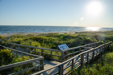 Wooden boardwalk crossing the sand dunes heading to the ocean. Oak Island NC beach in the background.