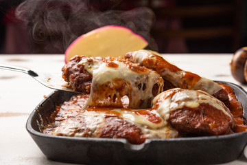 Parmegiana Steak also known as Filet Parmegiana in a black iron pan on a wooden white background,...