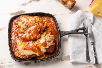 Parmegiana Steak also known as Filet Parmegiana in a black iron pan on a wooden white background, cheese and tomato sauce. Soft light, top view. Flat layer