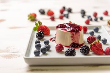 Delicious italian dessert panna cotta with berry sauce, fresh berries on white wooden background