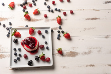 Delicious italian dessert panna cotta with berry sauce, fresh berries on white wooden background