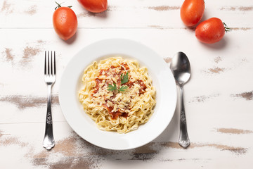 Fettuccine pasta with tomato sauce, parsley and basil in a white plate on a rustic wooden table background, soft light