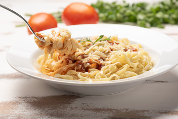 Fettuccine pasta with tomato sauce, parsley and basil in a white plate on a rustic wooden table background, soft light
