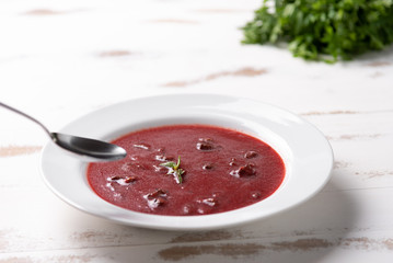 Delicious beet soup with sour cream in a white plate on white wooden table background. Soft light. Traditional Ukrainian Russian borscht beetroot soup
