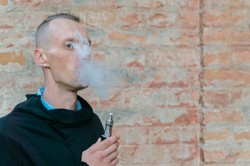 Vape man. Guy vaping electronic cigarette opposite vintage brick wall. Urban background with copy space. Lifestyle.