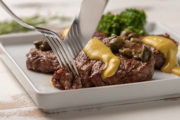 Filet mignon with caper and mustard sauce, broccoli, pepper grinder on wooden white background, soft light