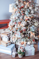 White decorated Christmas tree with many gifts underneath in gentle pastel colors. Good New Year spirit