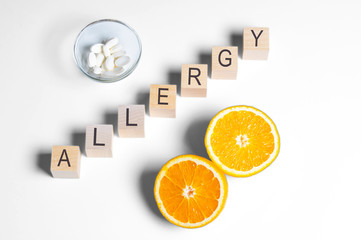 allergy. word from wooden blocks on a white background, citrus fruit, and Allergy pills