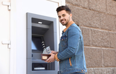 Young man with money near cash machine outdoors