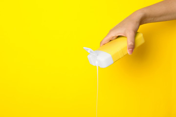 Woman pouring cosmetic product from bottle on yellow background, closeup. Space for text