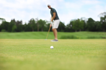 Man playing golf on green course, ball in focus