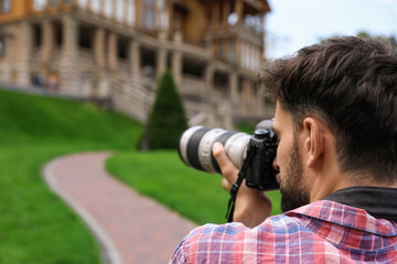 Photographer taking photo of beautiful house with professional camera outdoors