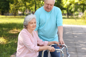 Elderly man helping his wife with walking frame outdoors