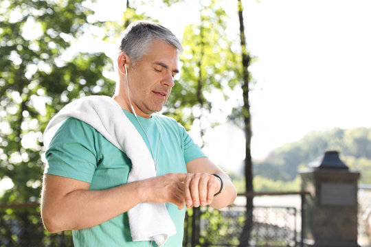 Handsome mature man looking at fitness tracker in park. Healthy lifestyle