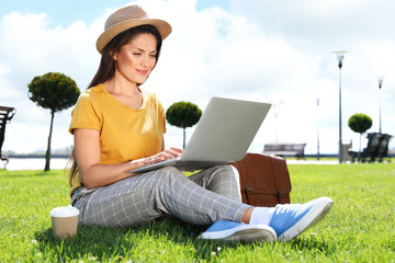 Beautiful woman with laptop sitting on green lawn outdoors