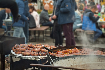 Barbecue fries in the coals. Blurred people eat at the table in the background. Meat and beef at...
