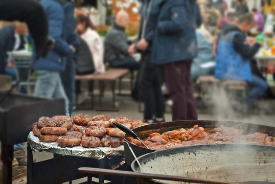 Barbecue fries in the coals. Blurred people eat at the table in the background. Meat and beef at the field kitchen festival.