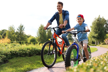 Fototapeta premium Dad and son riding modern bicycles outdoors