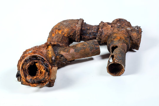Fragments of old cast-iron water pipes on white background. After many years of operation corroded metal pipe was destroyed. Rusty steel tube with holes of metallic corrosion. Rusty cast iron, metal