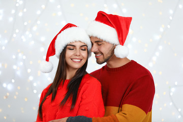 Lovely young couple in Santa hats against blurred festive lights. Christmas celebration