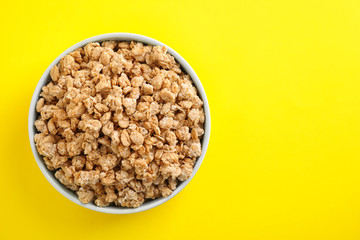 Bowl with healthy granola on yellow background, top view. Space for text