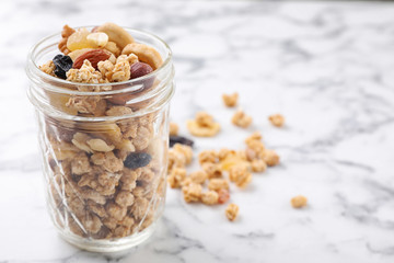 Jar with healthy granola on white marble table. Space for text