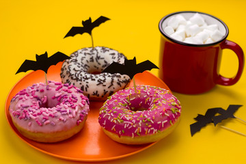 a plate with donuts decorated with paper cut bats and a mug of cocoa with marshmallows on the table...