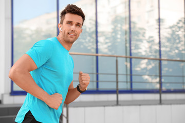 Young sportsman with wireless earphones running on city street