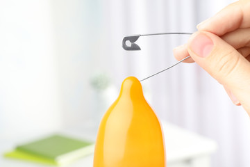 Woman piercing inflated condom with pin on blurred background, closeup. Safe sex