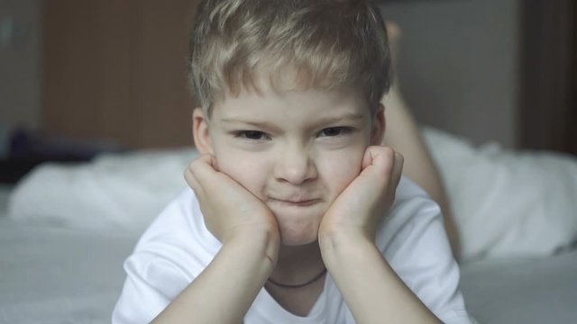 baby makes angry face close up in slow motion. boy's emotions. boy in a white t-shirt lying on the bed