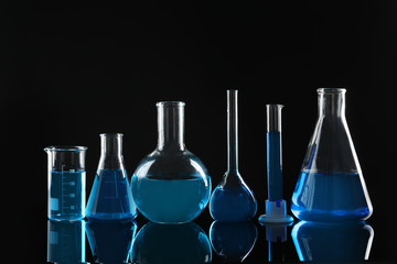 Laboratory glassware with blue liquids on black background